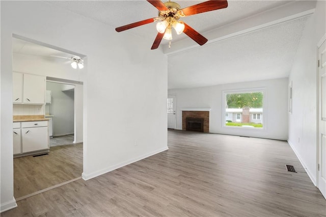 unfurnished living room with ceiling fan, a textured ceiling, light hardwood / wood-style flooring, and a brick fireplace