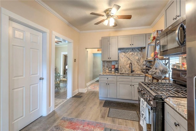 kitchen featuring appliances with stainless steel finishes, light wood-type flooring, ornamental molding, sink, and light stone counters