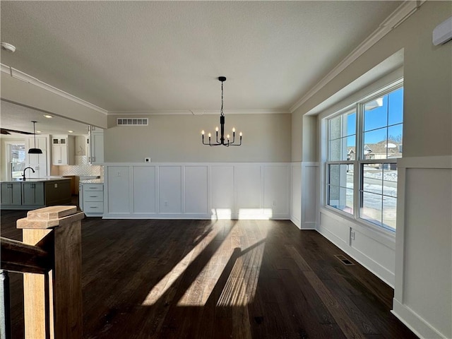 unfurnished dining area featuring sink, crown molding, a notable chandelier, and dark wood-type flooring