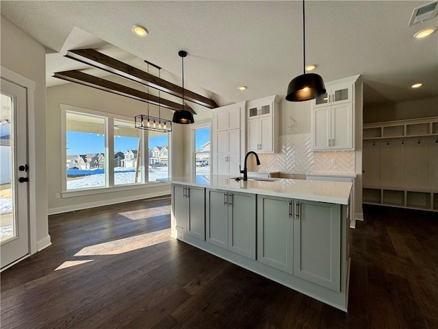 kitchen featuring white cabinets, pendant lighting, an island with sink, and beam ceiling