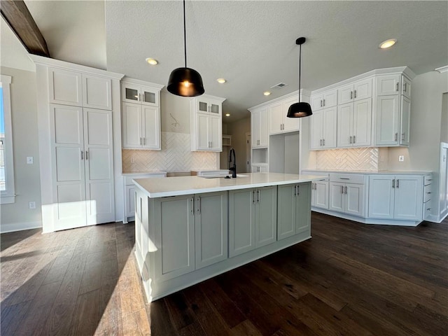 kitchen featuring dark wood-type flooring, pendant lighting, a kitchen island with sink, white cabinets, and sink