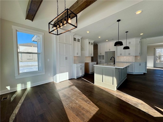 kitchen featuring white cabinetry, backsplash, beamed ceiling, and an island with sink