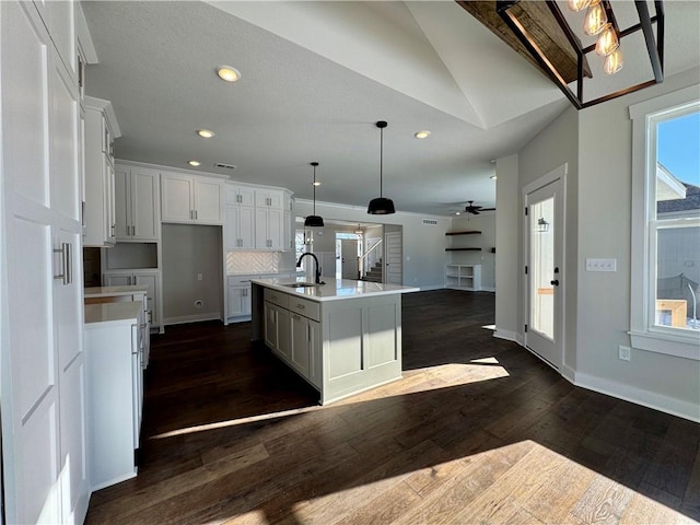 kitchen featuring a center island with sink, ceiling fan, pendant lighting, sink, and white cabinetry