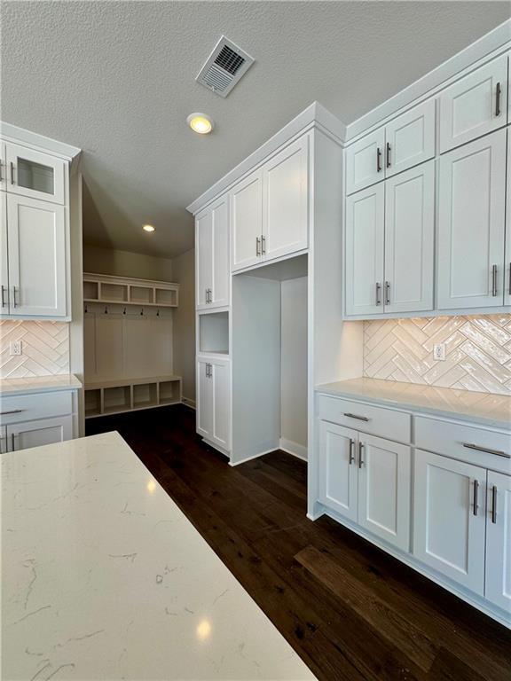 kitchen with light stone counters, a textured ceiling, dark hardwood / wood-style floors, decorative backsplash, and white cabinetry