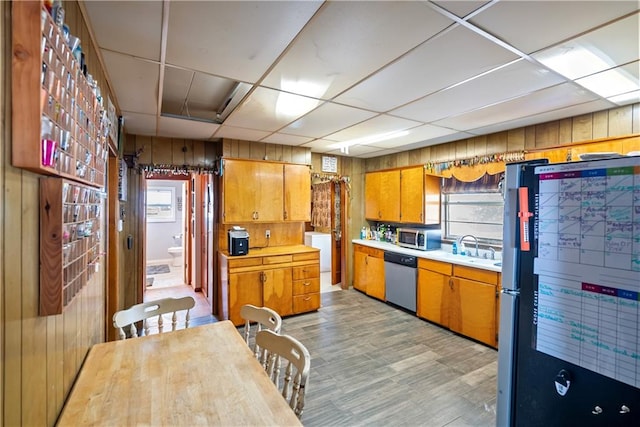 kitchen featuring appliances with stainless steel finishes, light hardwood / wood-style floors, wood walls, a drop ceiling, and sink