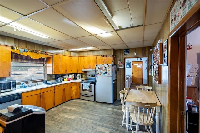 kitchen with a drop ceiling, wood walls, appliances with stainless steel finishes, and sink