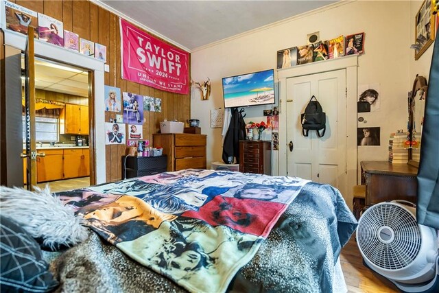 bedroom with ornamental molding, light hardwood / wood-style floors, and wooden walls