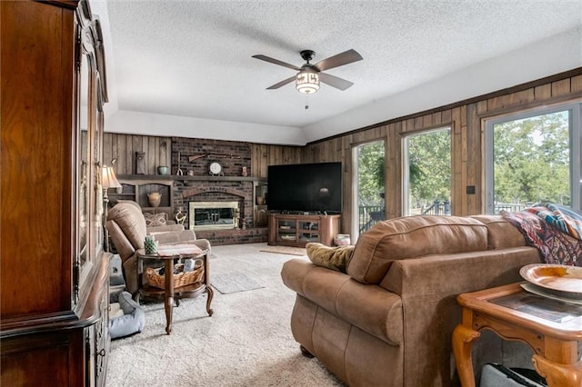 carpeted living room with a brick fireplace, ceiling fan, a textured ceiling, and wooden walls