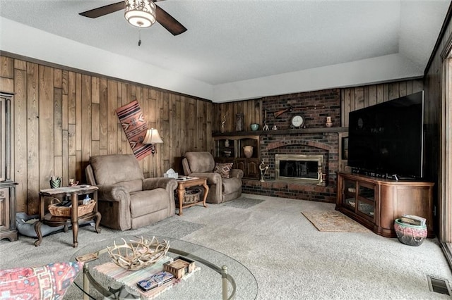 carpeted living room with wooden walls, vaulted ceiling, ceiling fan, and a fireplace