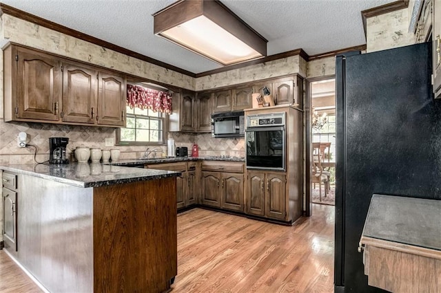 kitchen featuring dark stone counters, black appliances, ornamental molding, and light hardwood / wood-style flooring