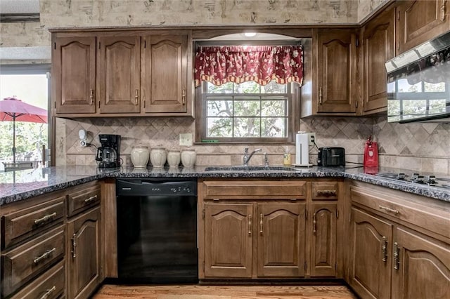 kitchen featuring light hardwood / wood-style floors, dark stone countertops, backsplash, black dishwasher, and sink