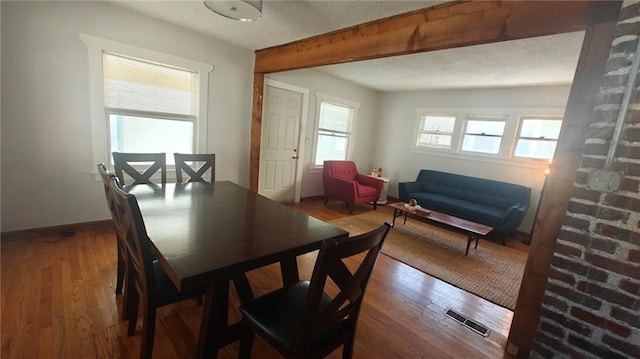 dining room with hardwood / wood-style floors, beamed ceiling, and a textured ceiling