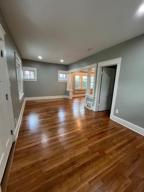 unfurnished living room featuring ornate columns, dark hardwood / wood-style flooring, and a wealth of natural light