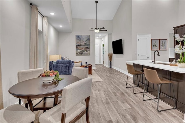 dining area featuring a high ceiling, light wood-type flooring, ceiling fan, and sink