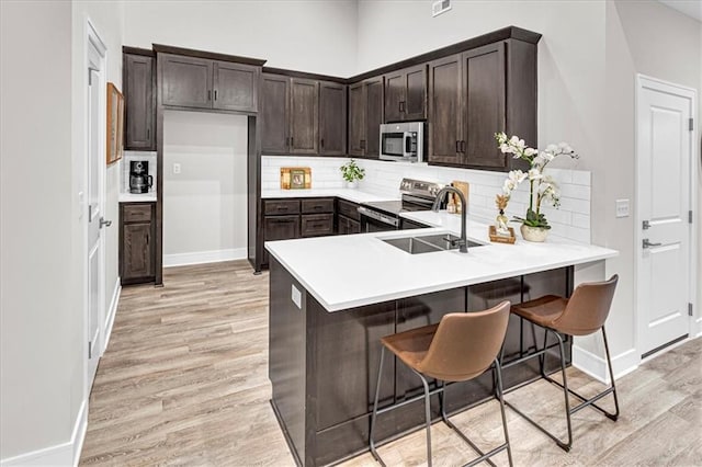 kitchen with a breakfast bar, kitchen peninsula, stainless steel appliances, and light hardwood / wood-style flooring