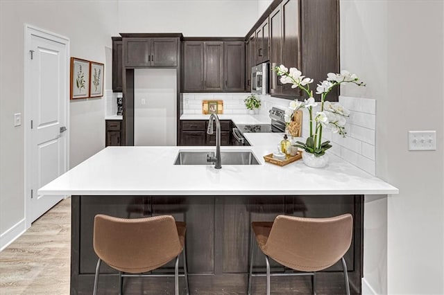 kitchen featuring a kitchen bar, appliances with stainless steel finishes, light wood-type flooring, kitchen peninsula, and sink