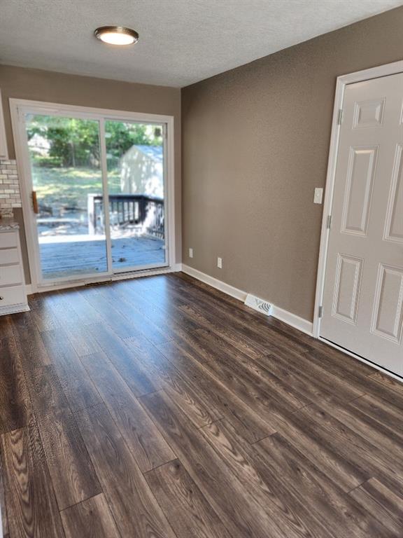 unfurnished room featuring a textured ceiling, a healthy amount of sunlight, and dark hardwood / wood-style flooring