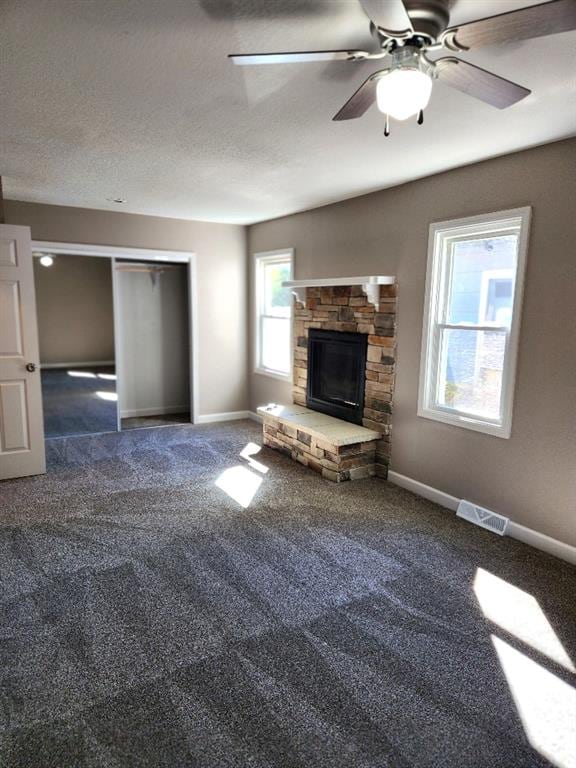 unfurnished living room featuring ceiling fan, a textured ceiling, a fireplace, and dark carpet