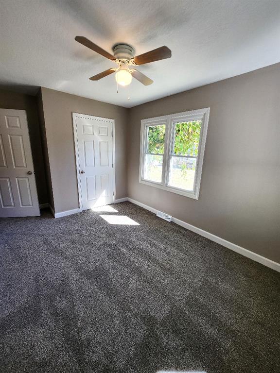 unfurnished bedroom featuring ceiling fan, a textured ceiling, and dark carpet