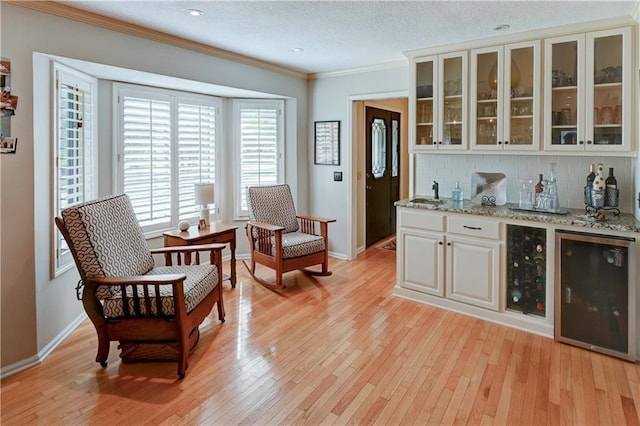 bar with wine cooler, sink, white cabinetry, light stone countertops, and crown molding