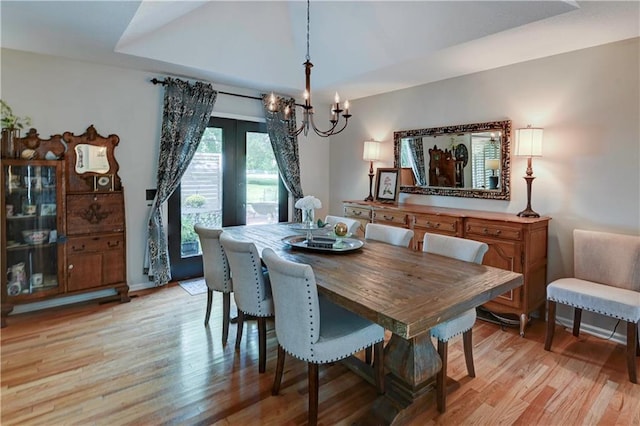 dining space with an inviting chandelier, light wood-type flooring, and a raised ceiling