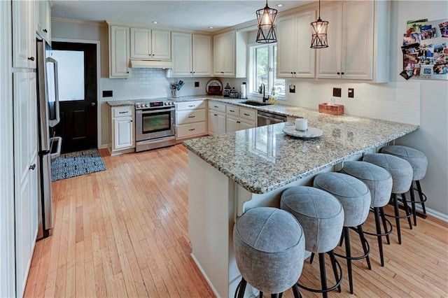 kitchen with a breakfast bar area, appliances with stainless steel finishes, decorative light fixtures, and kitchen peninsula