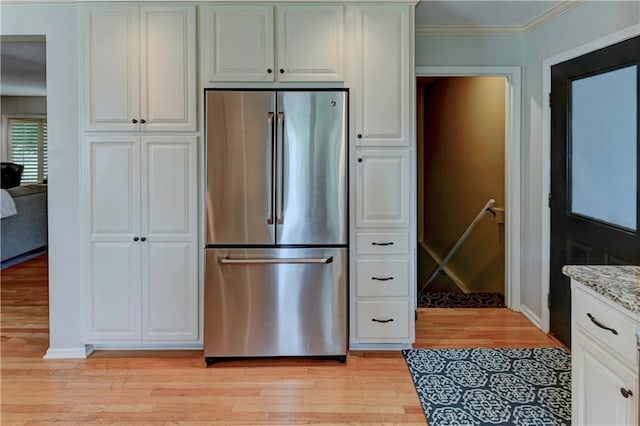 kitchen with stainless steel fridge, white cabinetry, light stone counters, light wood-type flooring, and crown molding