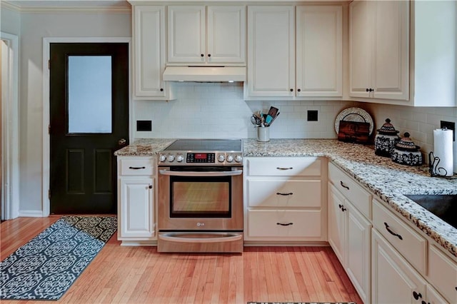 kitchen featuring light stone counters, stainless steel electric stove, light wood-type flooring, and backsplash