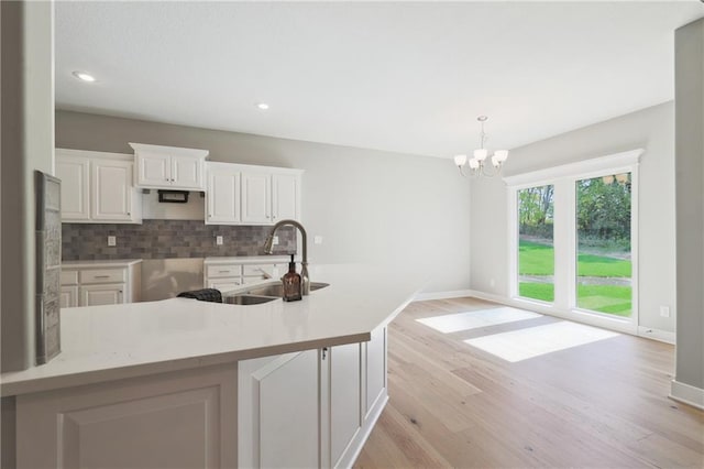 kitchen with white cabinets, sink, tasteful backsplash, light hardwood / wood-style flooring, and a chandelier