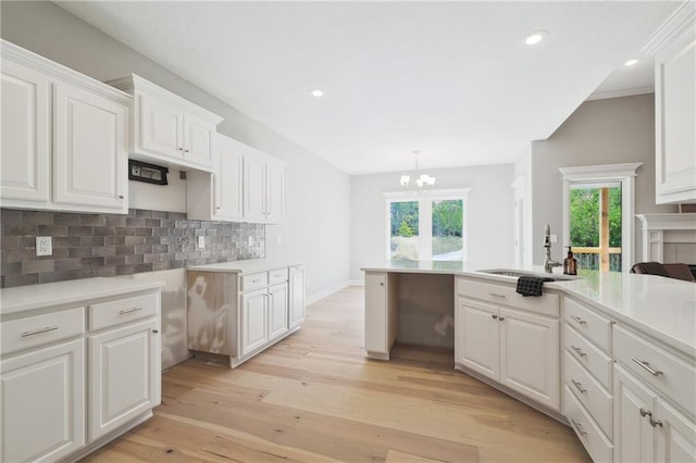 kitchen with decorative backsplash, white cabinetry, pendant lighting, light wood-type flooring, and sink