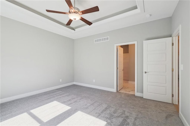 unfurnished bedroom with a raised ceiling, light carpet, ceiling fan, and a walk in closet