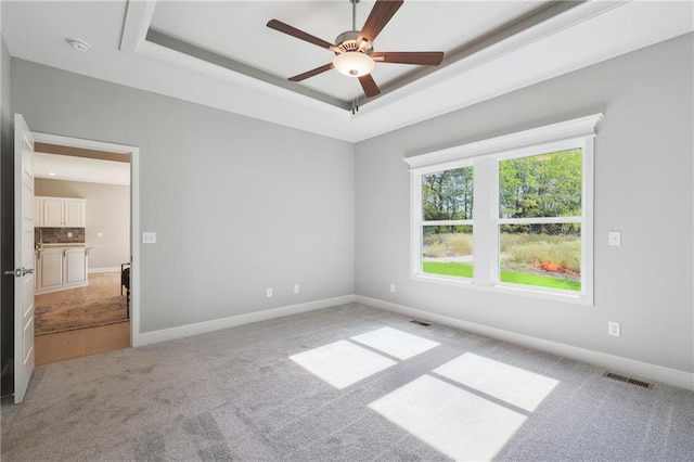 carpeted spare room with a tray ceiling and ceiling fan