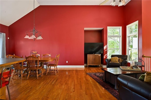 dining room featuring ceiling fan with notable chandelier, hardwood / wood-style floors, and high vaulted ceiling