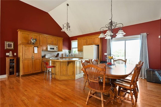 dining room with an inviting chandelier, a wealth of natural light, light hardwood / wood-style floors, and high vaulted ceiling