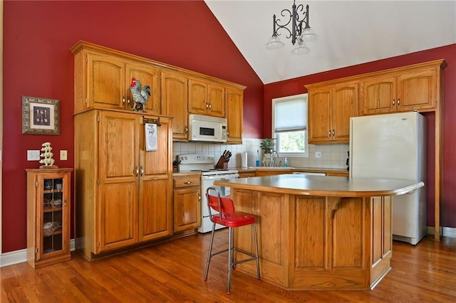 kitchen with a notable chandelier, hardwood / wood-style flooring, white appliances, and a center island