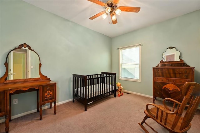 bedroom with light carpet, ceiling fan, and a crib