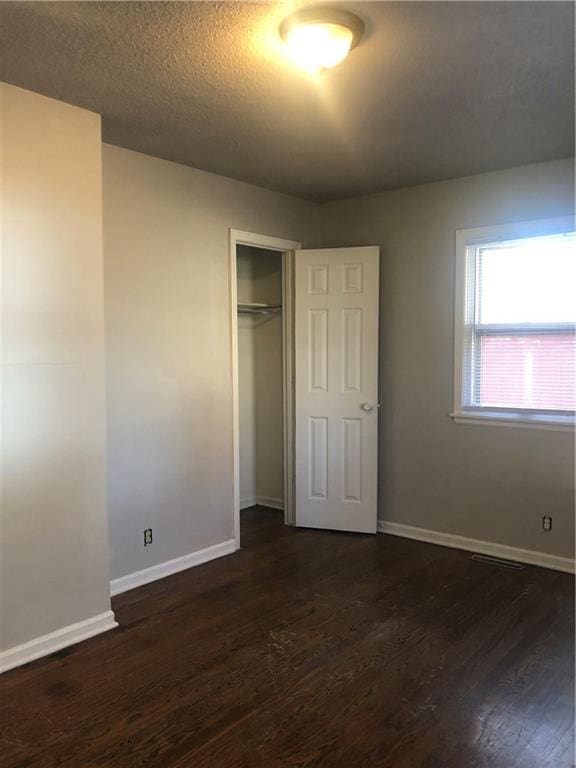 unfurnished bedroom featuring a textured ceiling, dark hardwood / wood-style floors, and a closet