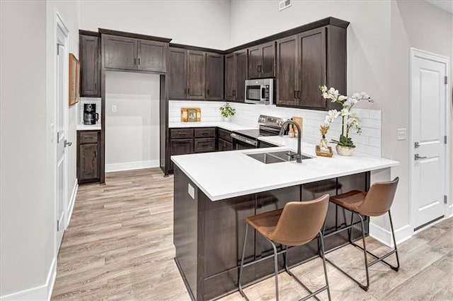 5830 Hunter Ct, Raytown, MO 64133 - kitchen with light wood-style flooring, tasteful backsplash, dark brown cabinets, a sink, and stainless steel appliances