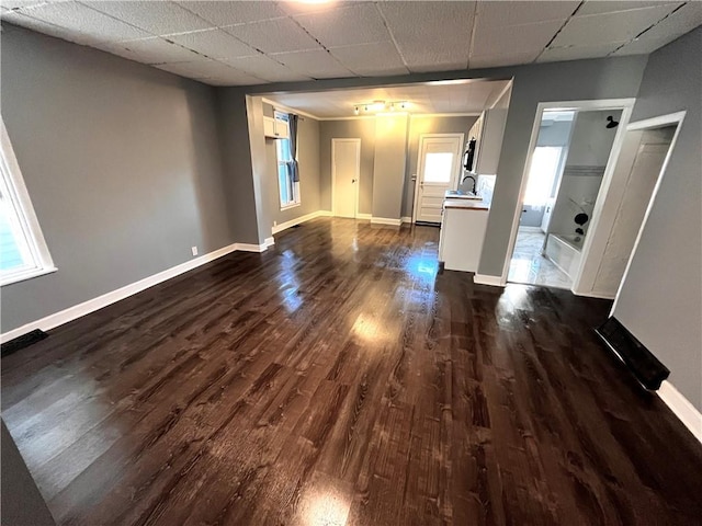 unfurnished living room featuring a drop ceiling, sink, and dark wood-type flooring