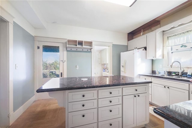 kitchen featuring dark stone countertops, sink, a center island, white refrigerator with ice dispenser, and white cabinets