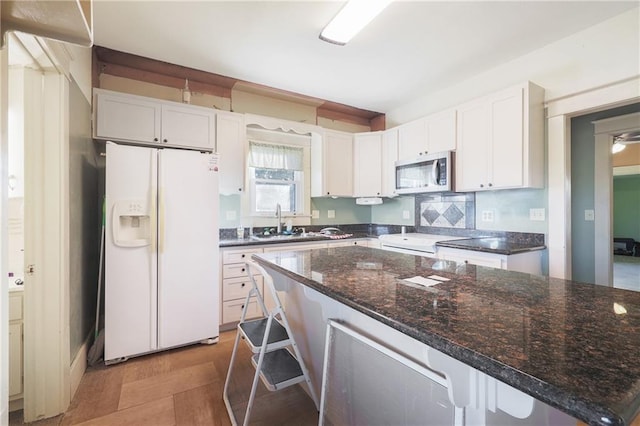 kitchen featuring sink, white fridge with ice dispenser, a breakfast bar area, and white cabinets