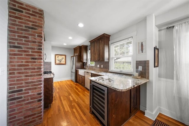 kitchen with light wood-type flooring, wine cooler, decorative backsplash, appliances with stainless steel finishes, and light stone countertops