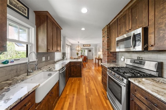 kitchen featuring pendant lighting, light wood-type flooring, light stone counters, tasteful backsplash, and appliances with stainless steel finishes