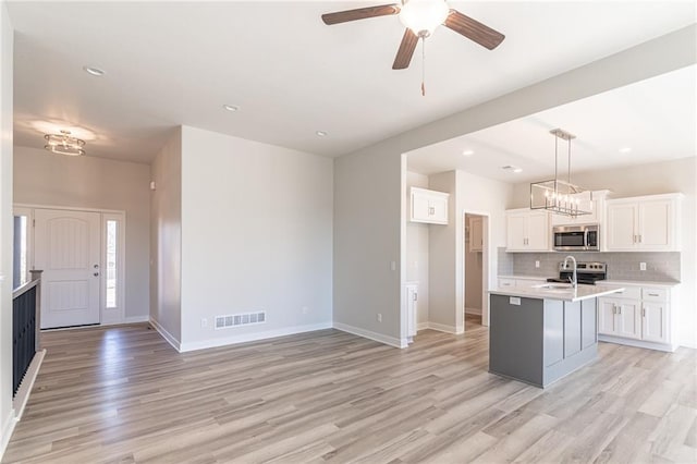 kitchen with light hardwood / wood-style floors, ceiling fan with notable chandelier, white cabinets, stainless steel appliances, and a center island with sink