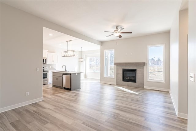 unfurnished living room featuring ceiling fan, a fireplace, sink, and light wood-type flooring