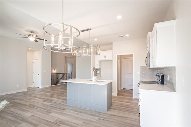 kitchen with sink, backsplash, white cabinets, a center island with sink, and decorative light fixtures