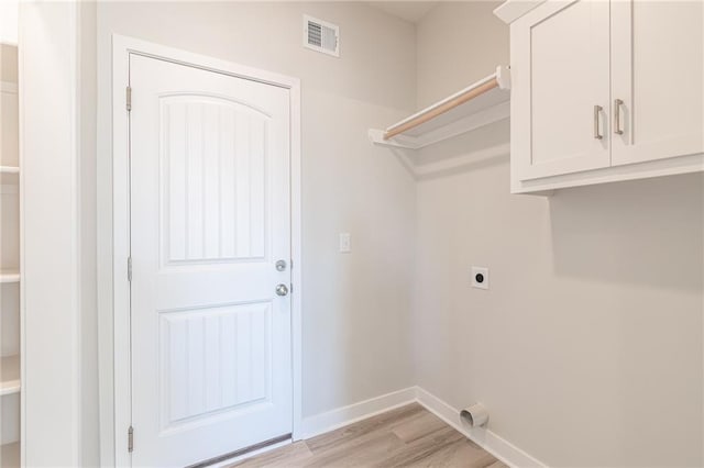 laundry area with electric dryer hookup, cabinets, and light wood-type flooring