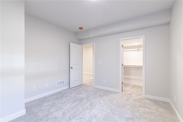 unfurnished bedroom featuring a walk in closet, light carpet, and a closet