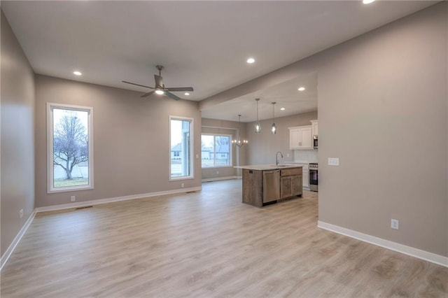 kitchen with decorative light fixtures, white cabinets, stainless steel appliances, a center island with sink, and light wood-type flooring