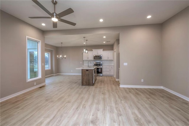 kitchen featuring appliances with stainless steel finishes, white cabinetry, tasteful backsplash, an island with sink, and decorative light fixtures